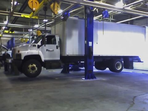 1992 Ford Bronco - A white box truck is raised on a hydraulic lift inside a garage or workshop.