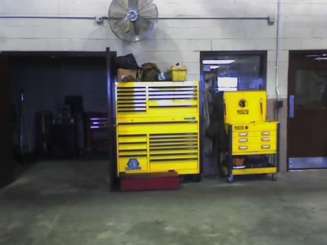 two yellow tool chests, one large and one smaller rolling cart, in a garage with a fan on the wall