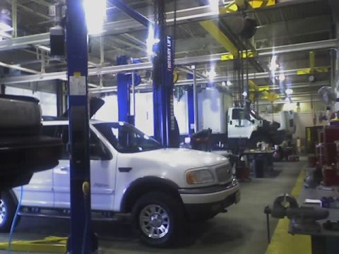 1992 Ford Bronco - A white Ford F-150 truck is parked in a repair bay with other vehicles and equipment visible.