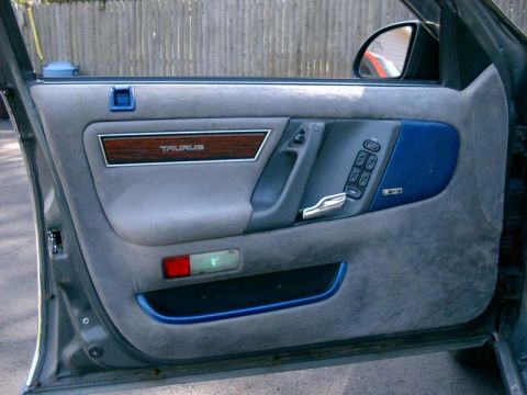 1986 Ford Taurus - Interior view of a 1986 Ford Taurus driver's side door panel, showing fabric upholstery and wood trim.