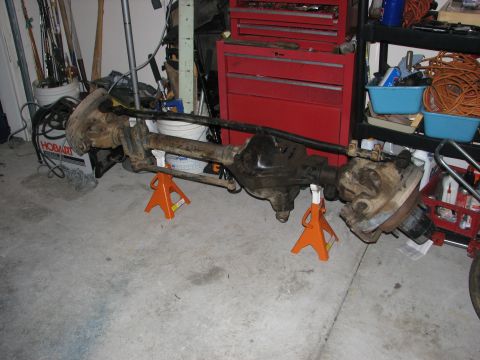 1984 Ford Bronco II - Front axle assembly, likely from a truck or SUV, is supported by orange jack stands in a garage setting.