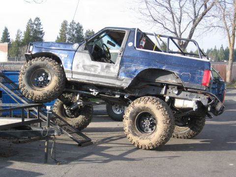 1994 Ford Bronco - This heavily modified SUV is positioned on a trailer ramp, with another vehicle visible in the background.