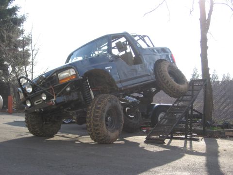 1994 Ford Bronco - A heavily modified 1994 Ford Bronco is shown with oversized tires, a custom bumper, and a roll cage, positioned on a ramp.