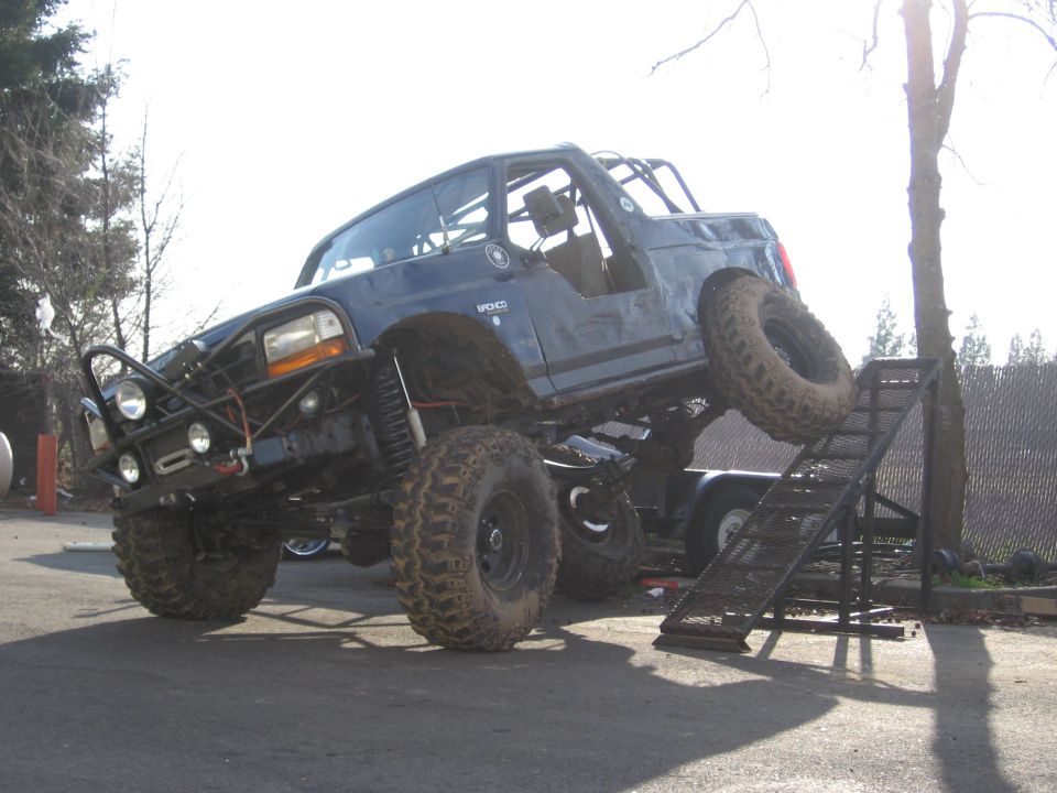 Blue caged Ford Bronco rock rig flexing on a trailer ramp with winch bumper