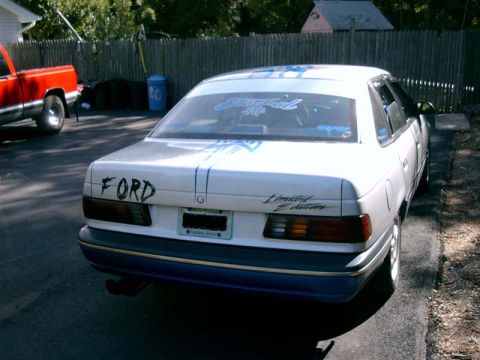 1986 Ford Taurus - A white 1986 Ford Taurus sedan is parked next to a red pickup truck.