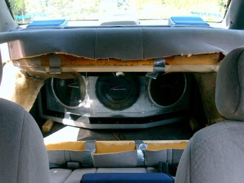 1986 Ford Taurus - Custom subwoofer installation in a vehicle's rear interior, with visible damage to the surrounding upholstery.