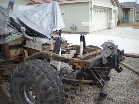 1982 Toyota 4Runner - The frame and suspension of a 1982 Toyota 4Runner are visible, with a large tire and a tarp covering part of the body.