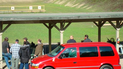 1990 Ford Bronco - A red minivan is visible at a shooting range with people standing under a covered area.