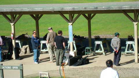 1990 Ford Bronco - People gathered at a shooting range under a covered shelter, with firearms visible on tables.