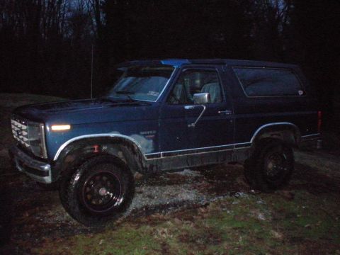 1986 Ford Bronco - This 1986 Ford Bronco is seen from a 3/4 front angle, parked outside in dim lighting.
