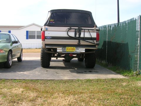 1996 Ford Bronco - The rear of a lifted 1996 Ford Bronco, a spare tire carrier and a yellow license plate, parked next to another vehicle.
