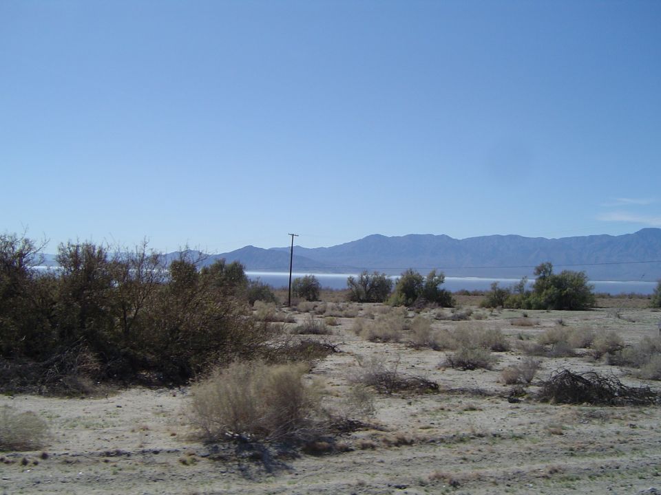 Desert landscape with mountains and a distant body of water under a clear blue sky