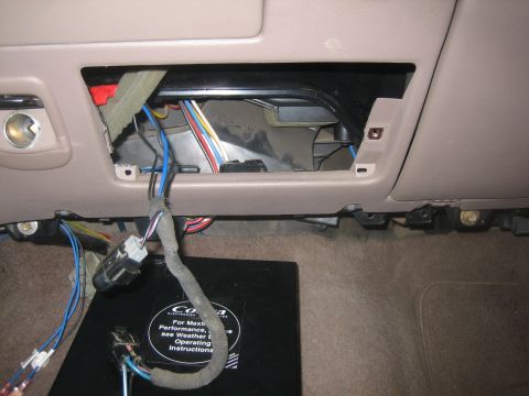 1995 Ford Bronco - Tan dashboard with the radio head unit removed, exposing the empty DIN opening and a bundle of blue, red and black wiring hanging out, rest…
