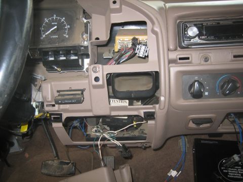 1995 Ford Bronco - Tan Ford truck dashboard partially disassembled, with trim bezels removed to expose the tachometer cluster, factory switch pack, rear-defro…