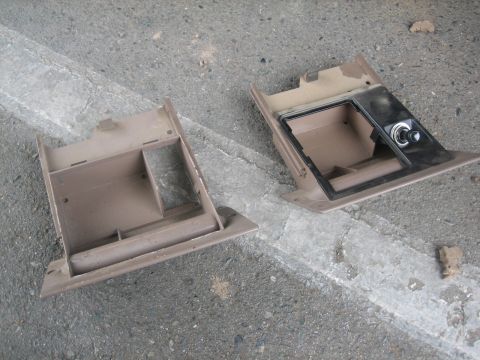 1995 Ford Bronco - Two removed tan plastic dash storage trays/pockets sitting upside down on a concrete driveway, one plain with internal dividers and the oth…