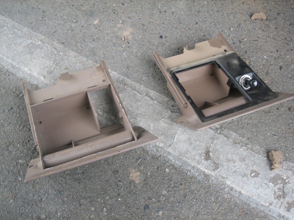 Two tan plastic dash storage trays removed and set on concrete, one with a chrome switch