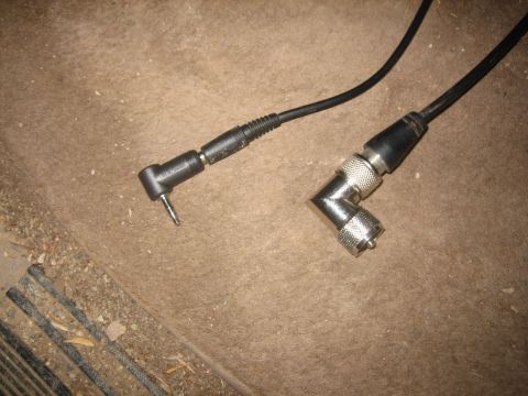 1995 Ford Bronco - Two coaxial antenna leads laid on a dirty tan carpeted floorboard: a small black right-angle Motorola-style radio antenna plug on the left…