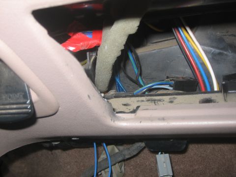 1995 Ford Bronco - Close-up inside an empty tan dash radio cavity showing loose blue, yellow, white, red and black wiring, a black plug connector, gray foam p…