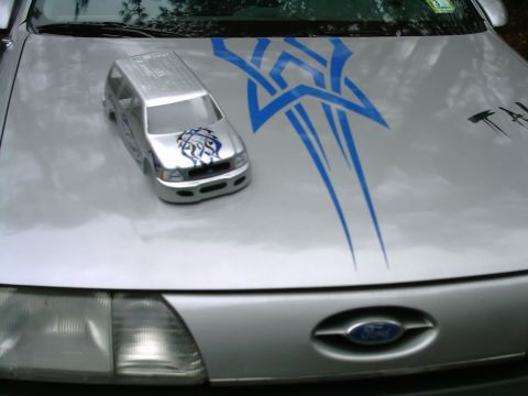1986 Ford Taurus - A toy SUV sits on the hood of a car adorned with tribal graphics.