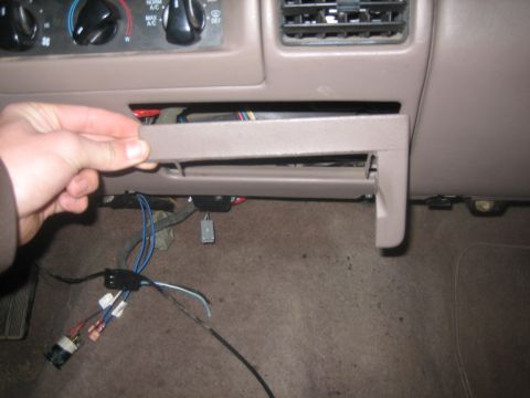 1995 Ford Bronco - A hand removes a small compartment from the dashboard, revealing wiring and carpet below.
