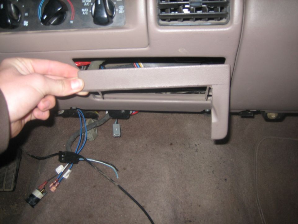 Dashboard panel with a hand removing a small compartment, exposing wires and carpet
