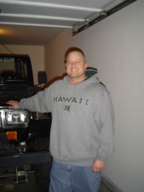 1989 Ford Bronco - A man poses for a photo in front of a Jeep Wrangler inside a garage.
