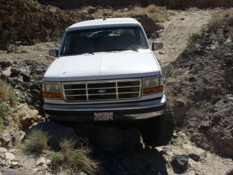 1993 Ford Bronco - A white Ford Bronco navigates a rough, rocky trail in a desert environment.