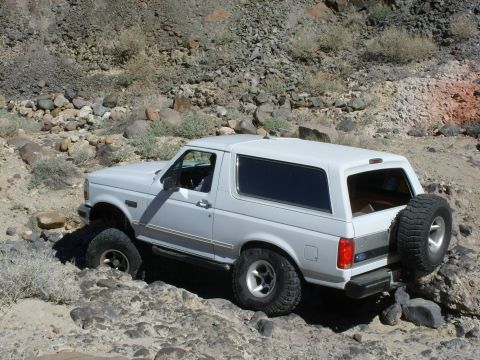 1993 Ford Bronco - White 1993 Ford Bronco tackles a challenging rocky path in a desert landscape.