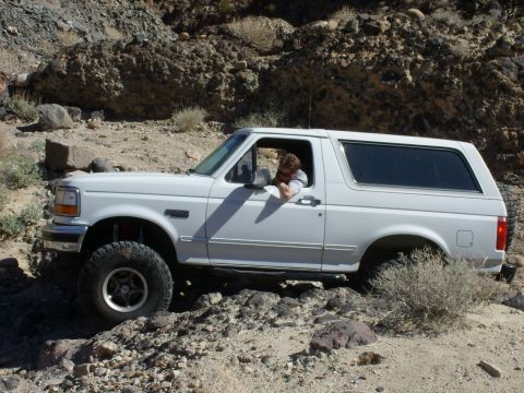 1993 Ford Bronco - A white Ford Bronco navigates a rough, rocky path in a desert landscape.