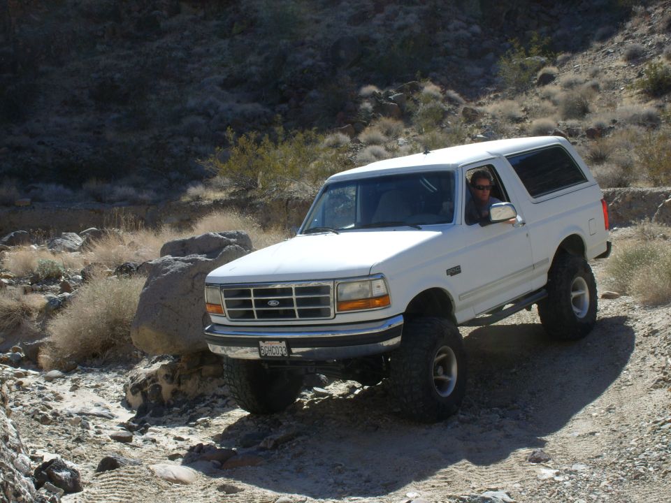 White lifted Ford Bronco parked at three-quarter front angle in rocky desert wash