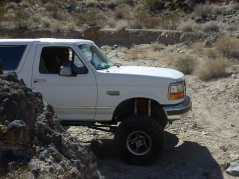 1993 Ford Bronco - White 1993 Ford Bronco navigates a rocky desert terrain with its suspension clearly visible.