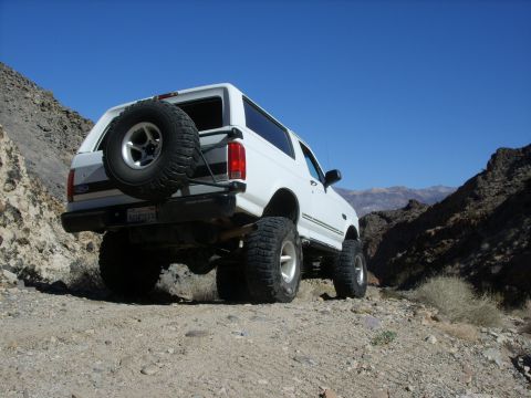 1993 Ford Bronco - White 1993 Ford Bronco with a lifted suspension and spare tire on the rear, navigating a rocky, mountainous terrain.