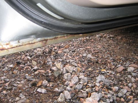 2001 Ford Crown Victoria - Close-up of a rusted vehicle door sill with gravel below.