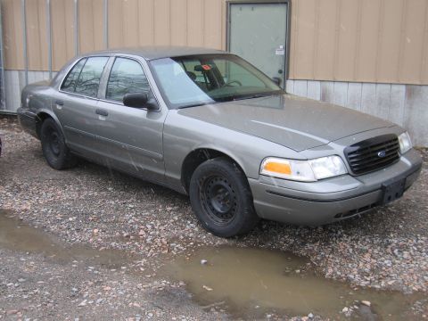 2001 Ford Crown Victoria - A gray 2001 Ford Crown Victoria is parked on a gravel lot with puddles.