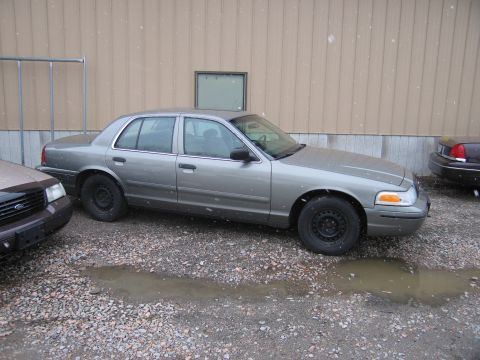 2001 Ford Crown Victoria - A gray 2001 Ford Crown Victoria sedan is parked next to another vehicle on a gravel lot.