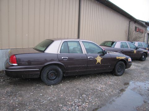 2001 Ford Crown Victoria - Three dark brown Ford Crown Victoria police cars with tan roofs are parked outside a building.