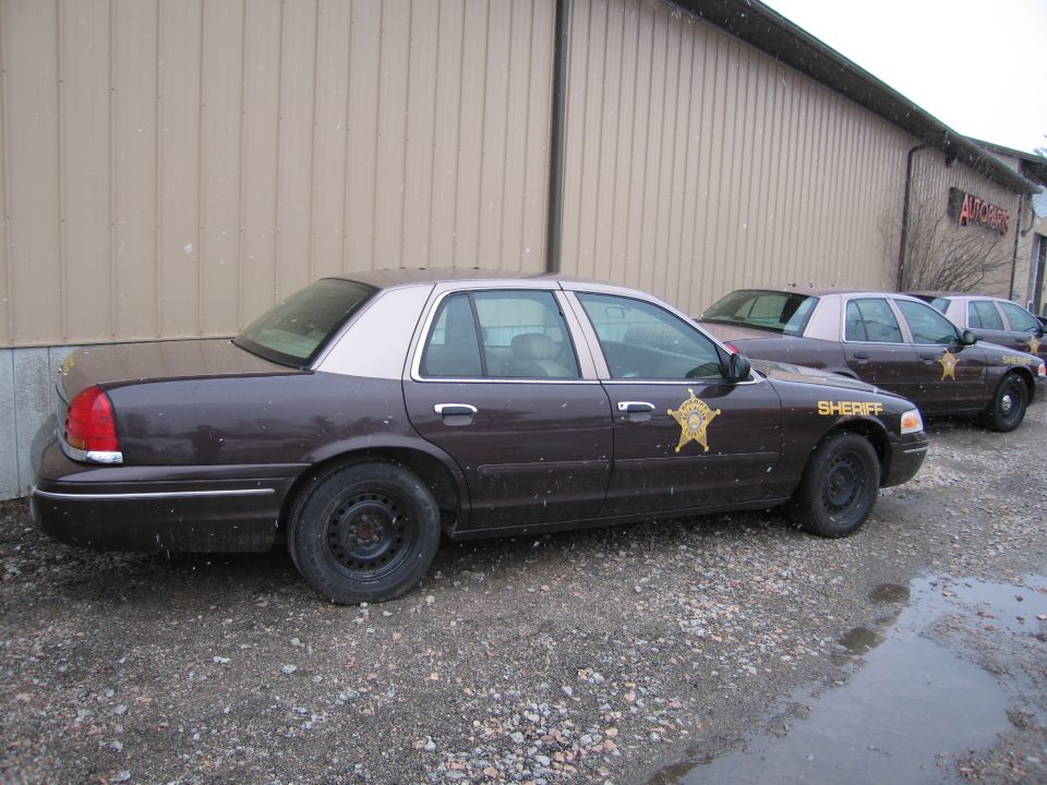 Dark brown 2001 Ford Crown Victoria police car with tan roof, side view, parked on gravel
