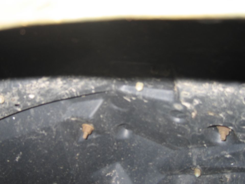 Black plastic wheel well liner with visible rust spots and screws