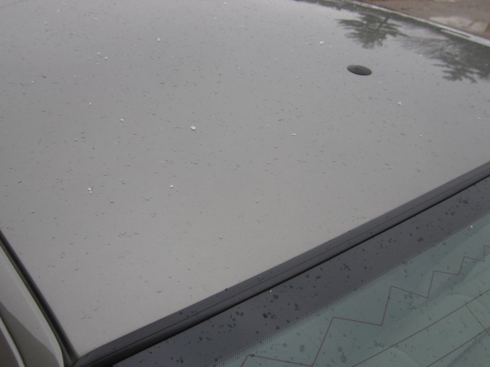 Gray car roof with water droplets and a small black antenna base