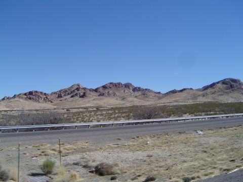 1989 Ford Bronco - A wide view of a desolate desert highway stretching towards mountains under a bright blue sky.
