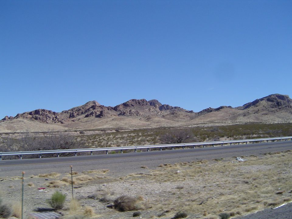 Desert landscape with mountains and a highway under a clear blue sky