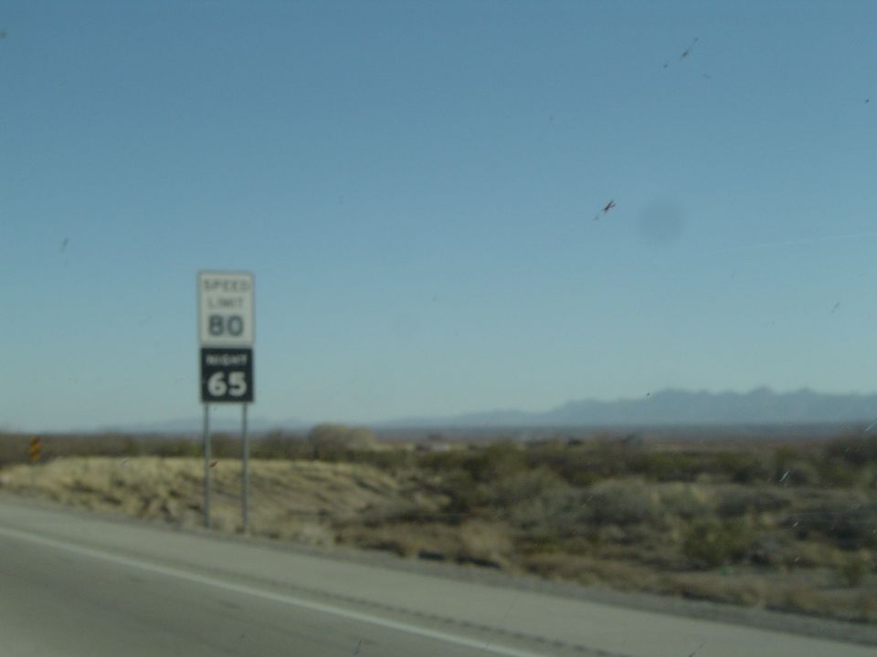 Speed limit sign showing 80 and 65, next to a highway with desert landscape