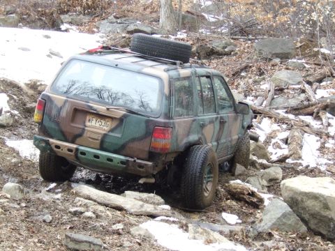 1976 Toyota Land Cruiser - Camouflage Jeep Grand Cherokee navigates a challenging rocky trail with snow patches.
