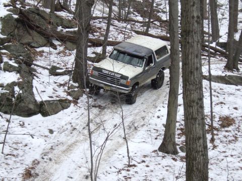 1976 Toyota Land Cruiser - Ford Bronco navigates a snowy, wooded terrain. The vehicle appears to be from the late 1980s.