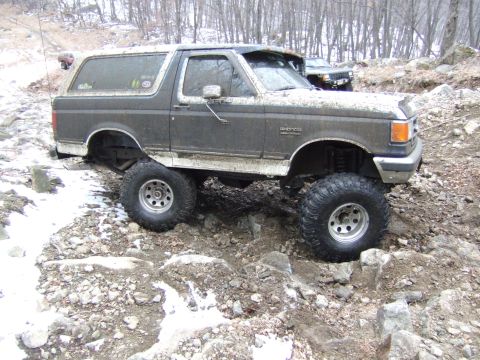 1976 Toyota Land Cruiser - A modified Ford Bronco tackles a challenging off-road course with another vehicle visible in the background.
