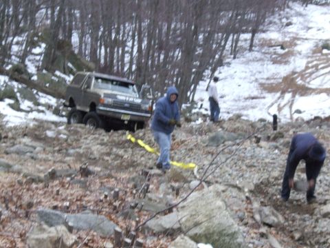 1976 Toyota Land Cruiser - A Ford Bronco is stuck on a rocky incline, with several people attempting to assist.