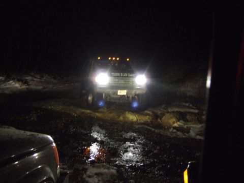 1976 Toyota Land Cruiser - A dark SUV drives through a muddy, wet area at night, its headlights illuminating the path.