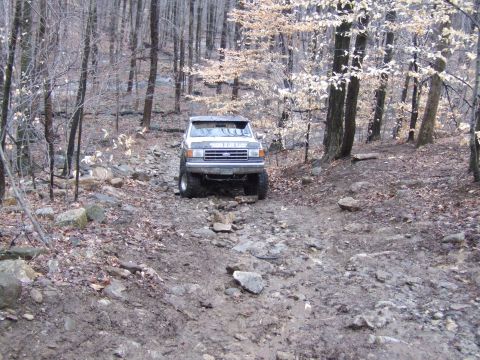 1976 Toyota Land Cruiser - A white pickup truck navigates a challenging off-road course through a wooded area.