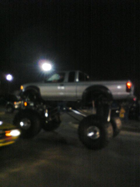 2001 Nissan Frontier - A silver pickup truck is heavily modified with a lift kit and massive tires, seen at night.