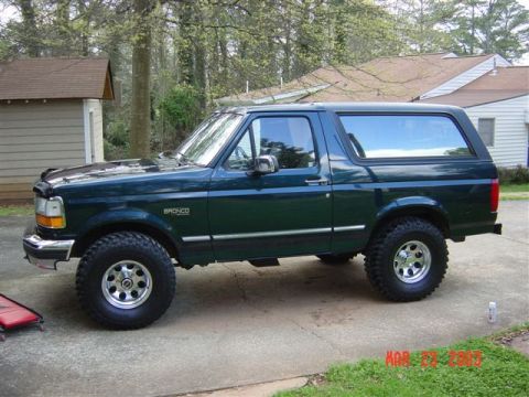 1995 Ford Bronco - This 1995 Ford Bronco features a dark green exterior and aftermarket wheels, viewed from the side.